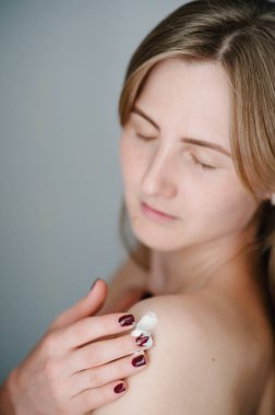 Çekici, güzel bir kadın, duştan sonra vücuduna nemlendirici krem sürüyor. Gri arka planda kusursuz cilde sahip genç bir kızın fotoğrafı. Kapatın. Cilt bakımı ve güzellik kavramı.