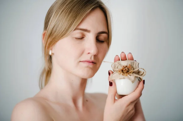 Photo of young girl with flawless skin. Smiling woman holding little jar of skin cream and applying bottles lotion, natural cosmetics. Cosmetology, beauty and spa. Wellness. Close up.