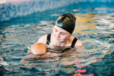 Kürek havuzuna bebek dalışı. Genç anne, yüzme öğretmeni ve bilardodaki mutlu küçük kız. Küçük çocuğa yüzmeyi öğret. Suda yüzmenin ilk gününün tadını çıkar. Anne bebeği tutuyor ve dalıyor.