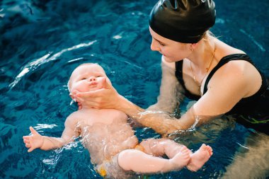 Genç anne, havuzda mutlu küçük kız. Çocuğa yüzmeyi öğretiyor. Suda yüzmenin ilk gününün tadını çıkar. Annem çocuğu dalış için hazırlıyor. Egzersiz yapıyorum. Çocuğu suya götüren el.