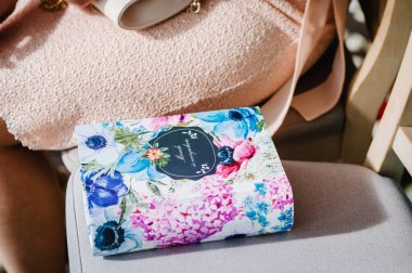 Kitap, bir kadının yanındaki sandalyede renkli çiçeklerle süslenmiş. Her yerde ismi ve mesajı olan bir kutu şeklinde bir hediye var. Kapat..