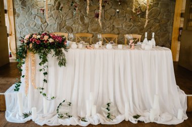 Çiçek ve yeşillik kompozisyonu ile süslenmiş şölen masası, düğün salonundaki mumlar. Yeni evliler masa örtüsüyle kaplanmış, tabak ve çatal bıçakla servis ediliyor. Kapat..