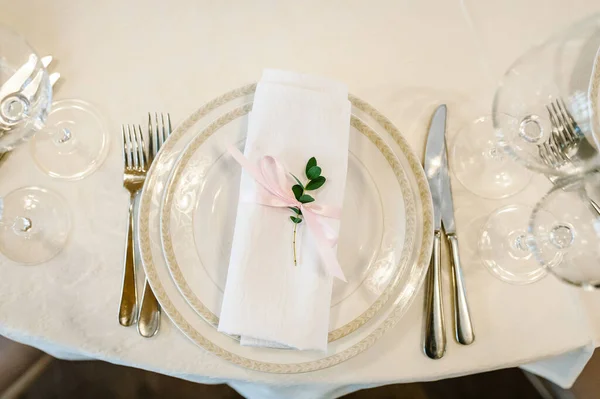 Serving, setting table. Two plates and silverware cutlery  linen napkin are decorated with pink ribbons and branch greens. Wedding table decoration. Artwork. flat lay. top view. Close up.