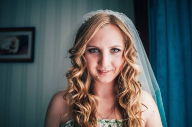 Kıvırcık saçlı, gülümseyen güzel sarışın kız. Yeşil giysili beyaz elbise. Günaydın Gelin. - Hanımefendi. Arka planda mutlu. Kafasındaki duvak. Makyaj, saç. Kapatın. Güzel yeşil gözler.