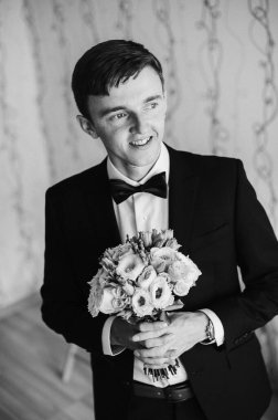 Mutlu damat ayakta duruyor ve poz veriyor. Düğün sabahı. Kapat. Geçmişi. Gülümse, portre. Elinde bir buket gül. siyah ve beyaz