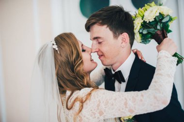 Bir buket düğün çiçeğiyle görkemli zarif bir gelin damadın burnuna dokunup sarılıyor. Duvarın arka planında. Portre 'yi kapat. Geçmişe dönüş. Kapalı Mimari