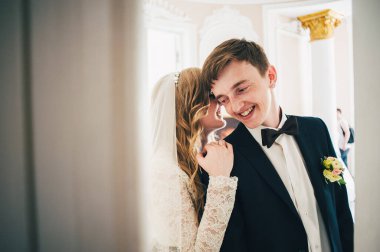 Muhteşem şık, zarif bir gelin ayağa kalkar ve damatınkine dokunur ve sarılır. Duvarın arka planında. Kapatın. Portre. Geçmişe dönüş. Kapalı alanda. Mimarlık. Kapıdan çık..