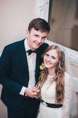 Zarif, zarif bir gelin ve damat aynanın yanında duruyor. Önüne bak. El ele tutuşun Sarılalım. Kapatın. Geçmişe dönüş. Kapalı alanda klasik mimari. Yeni evlilerin portresi.