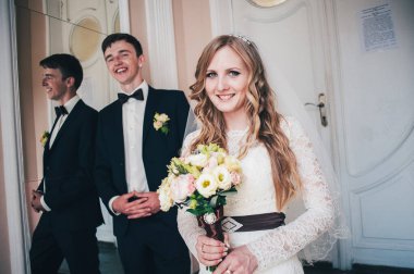 Zarif, zarif bir gelin ve damat ayna ve kapıların yanında duruyor. Önüne bak. El ele tutuşun Düğün buketine sarılıyor. Kapatın. Geçmişe dönüş. Kapalı alanda klasik mimari. Yeni evlilerin portresi.