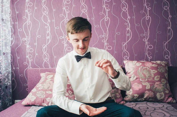 Elden ele alyansları atın. Kanepede oturup poz veren mutlu damat. Düğün sabahı. Kapat. Menekşe arkaplanda. Gülümse, portre