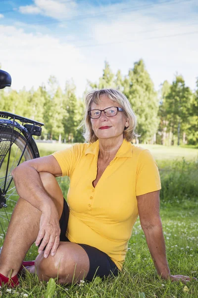 Retrato de una mujer mayor sonriente sentada en el parque con bicicleta —  Fotos de Stock
