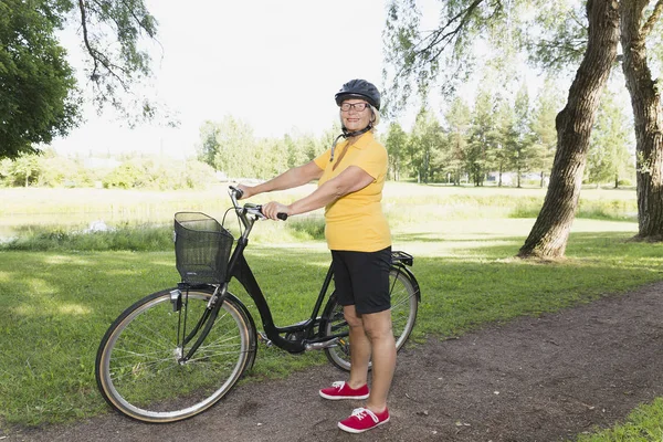 Donna anziana in bicicletta in un parco nel pomeriggio di sole — Foto Stock