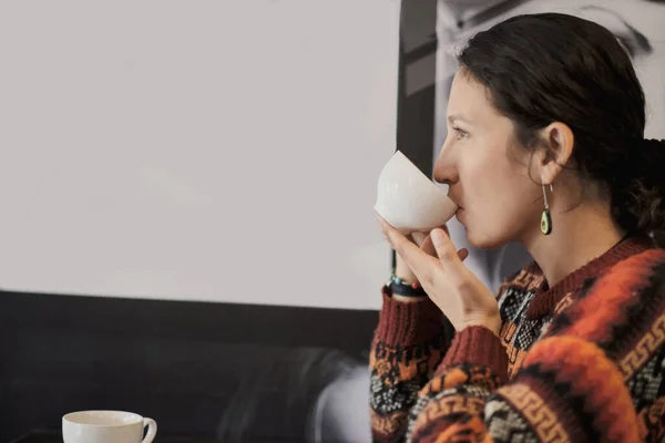 Woman drinks hot drink from a white cup. Profile woman