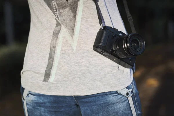 Photo of a black professional camera. Woman with gray blouse holds a camera