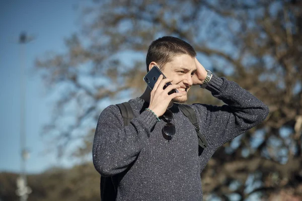 Casual young man speaks on the phone and holds his hand over his head.
