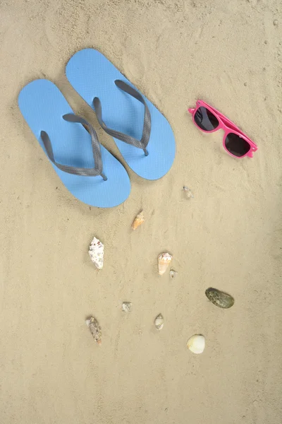Chanclas azules, gafas de sol y conchas marinas en la arena — Foto de Stock