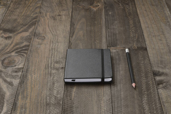 Черный блокнот закрыт резиной и ручкой на деревянном фоне
