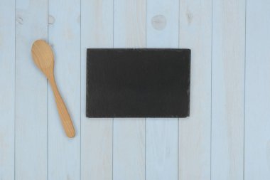 Mutfak eşyaları: ahşap kaşık ve mavi ahşap arka planda siyah taş plaka.