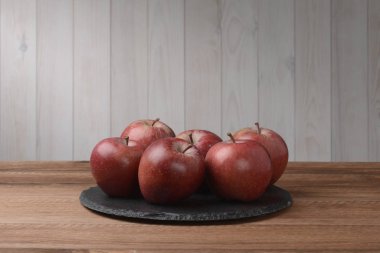 Elmalar yuvarlak siyah bir tabakta kahverengi ahşap masa ve beyaz duvar