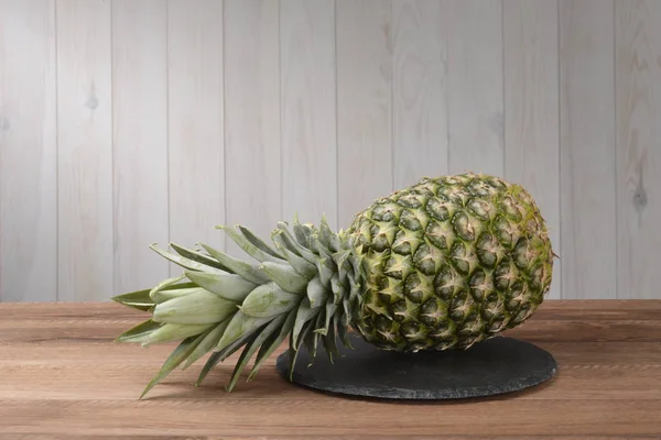 Pineapple on a round black slate dish on brown wooden table and white wall