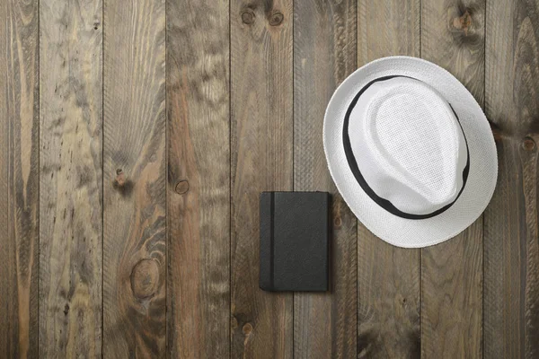White hat and black notebook on wooden background — Stock Photo, Image