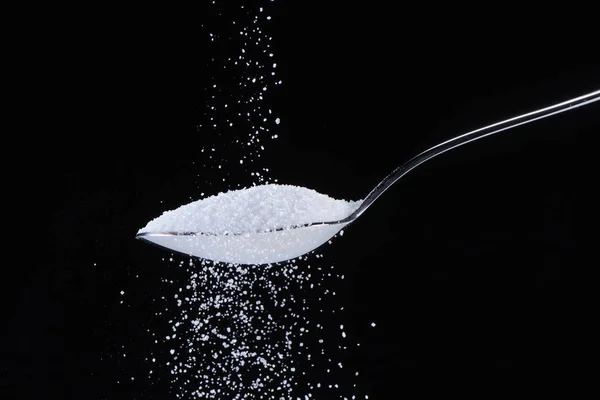 Socker faller i en sked på svart bakgrund — Stockfoto