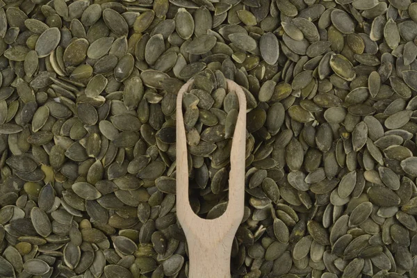 Peeled pumpkin seeds and a wooden spoon — Stock Photo, Image