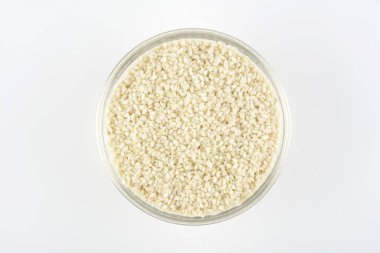 Beyaz arka planda cam bir kasede beyaz susam tohumu, üst manzara