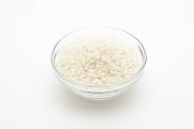 Beyaz arka planda cam bir kasede çiğ pirinç.