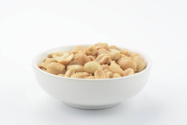 Beyaz arka planda beyaz seramik kasede kızartılmış kabuklu fıstıklar.