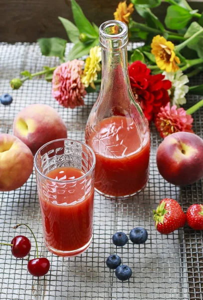 Bottle and glass with red juice, cherries, blueberries and peach — Stock Photo, Image