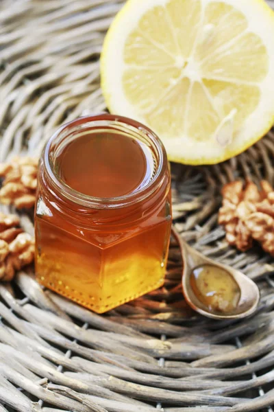 Jar of honey on wicker tray, lemon and nuts in the background. — Stock Photo, Image