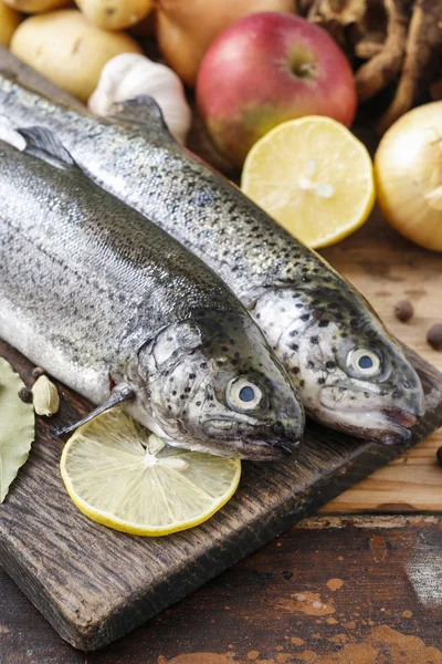 Two rainbow trouts on rustic wooden table among herbs and vegeta — Stock Photo, Image