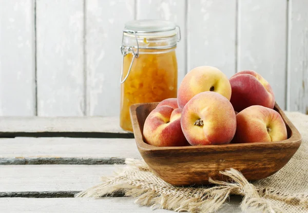 Skål med persikor och burk sylt på träbord. — Stockfoto