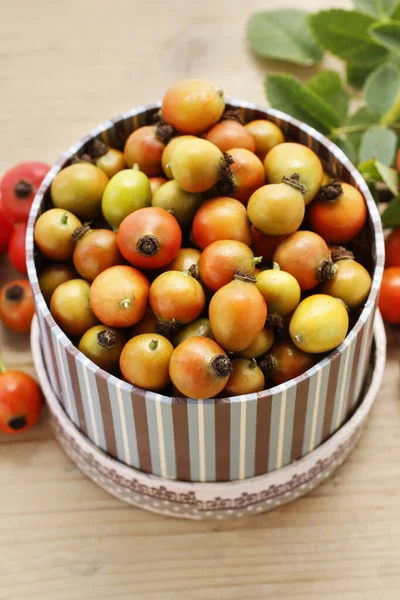 Vintage striped box of rose hip fruits on wooden table.