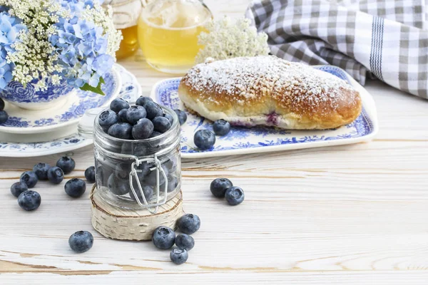 Jar with blueberries and fresh bun on white wooden table — ストック写真