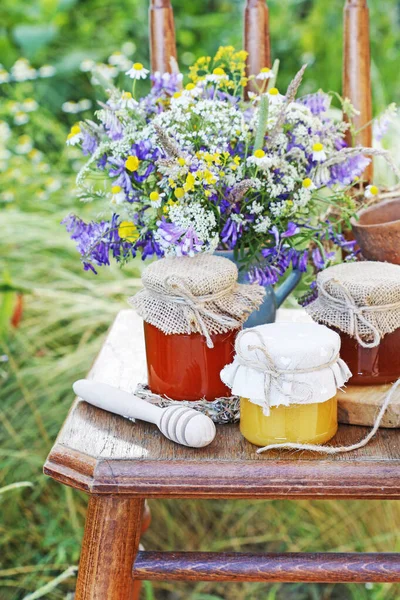 Vasi con miele e bouquet di fiori selvatici in giardino . — Foto Stock