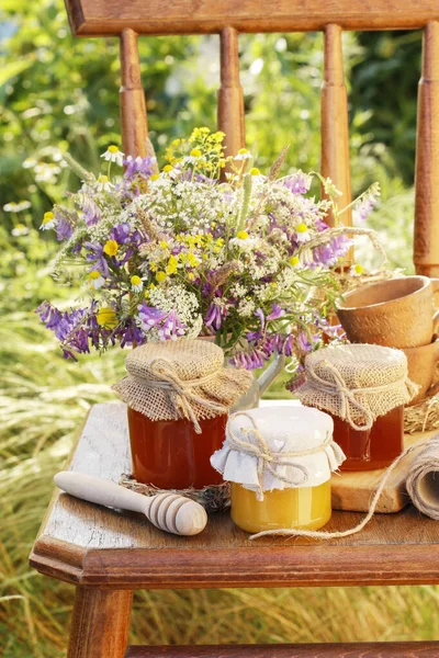 Vasi con miele e bouquet di fiori selvatici in giardino . — Foto Stock