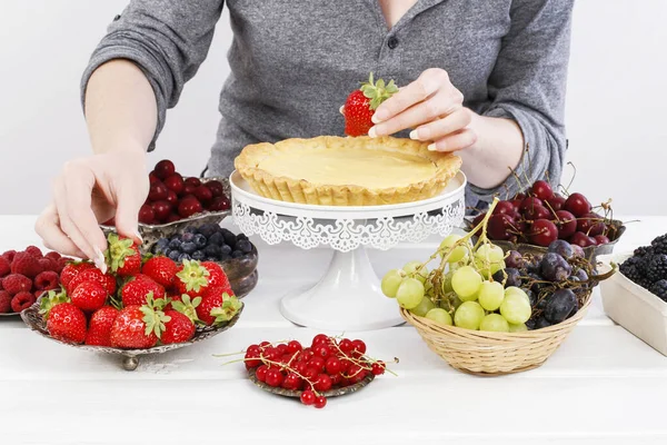 Kvinna dekorerar en stor tårta med olika frukter. — Stockfoto
