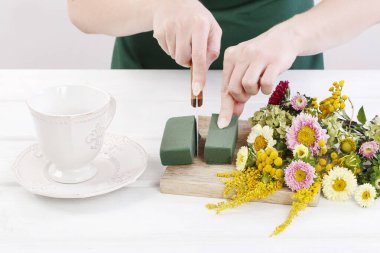 Kadın, yaz çiçekleriyle nasıl çiçek aranjmanı yapılacağını gösteriyor.