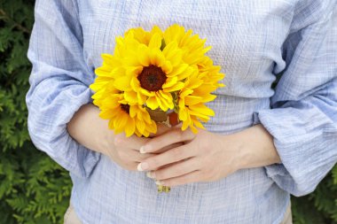 Kadın elinde bir buket ayçiçeği tutuyor..