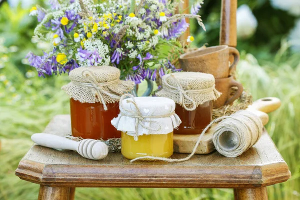 Jars with honey and bouquet of wild flowers in the garden. — Stock Photo, Image