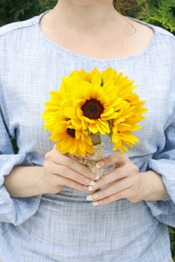 Kadın elinde bir buket ayçiçeği tutuyor..