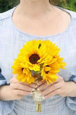 Kadın elinde bir buket ayçiçeği tutuyor..