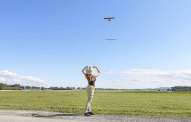Şapkalı genç bir kadın bir uçağa ve planöre bakıyor. 