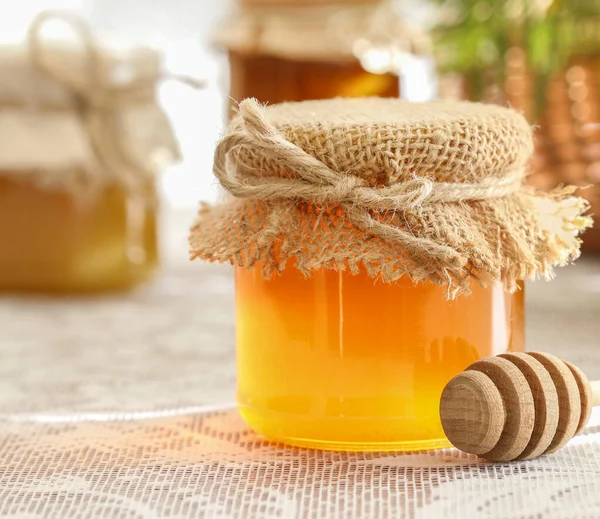 Gläser mit Honig auf dem Tisch und Sonnenblumen im Hintergrund — Stockfoto