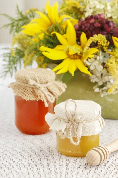 Toples kaca dengan madu di atas meja dan bunga matahari di backgro — Stok Foto