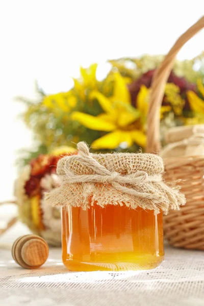 Toples kaca dengan madu di atas meja dan bunga matahari di backgro — Stok Foto