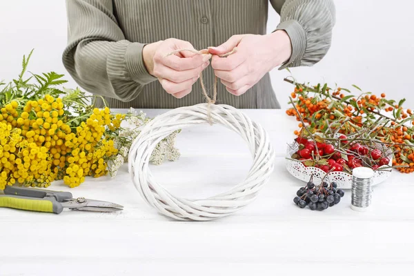 Frau zeigt, wie man mit Hagebutte, Stiefmütterchen und Co. einen Herbstkranz macht — Stockfoto