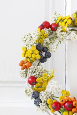 Beyaz ahşap üzerinde gül kalçası, tansi ve spiraea ile sonbahar çelengi